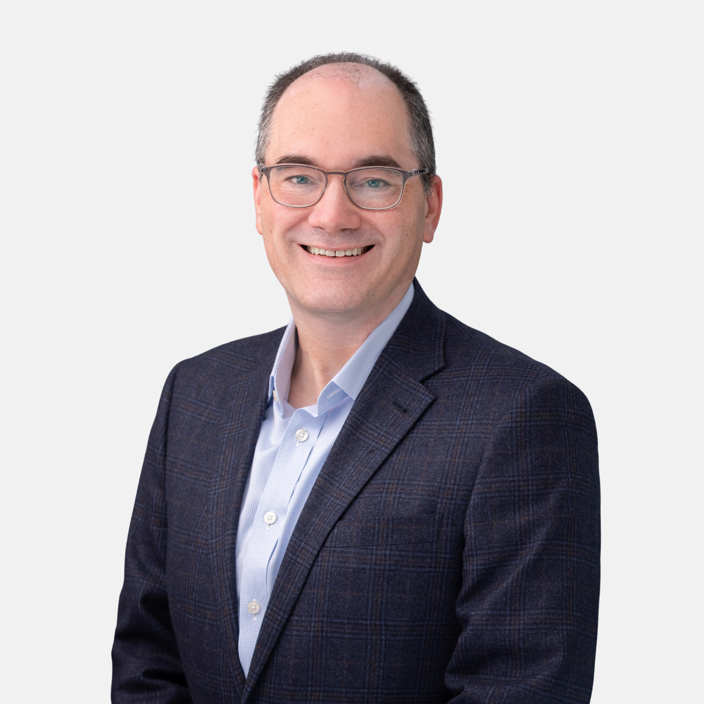 Headshot of Benjamin C. Eggert with short brown hair and glasses, wearing a dark patterned blazer and open-collar light blue shirt, smiling against a light background