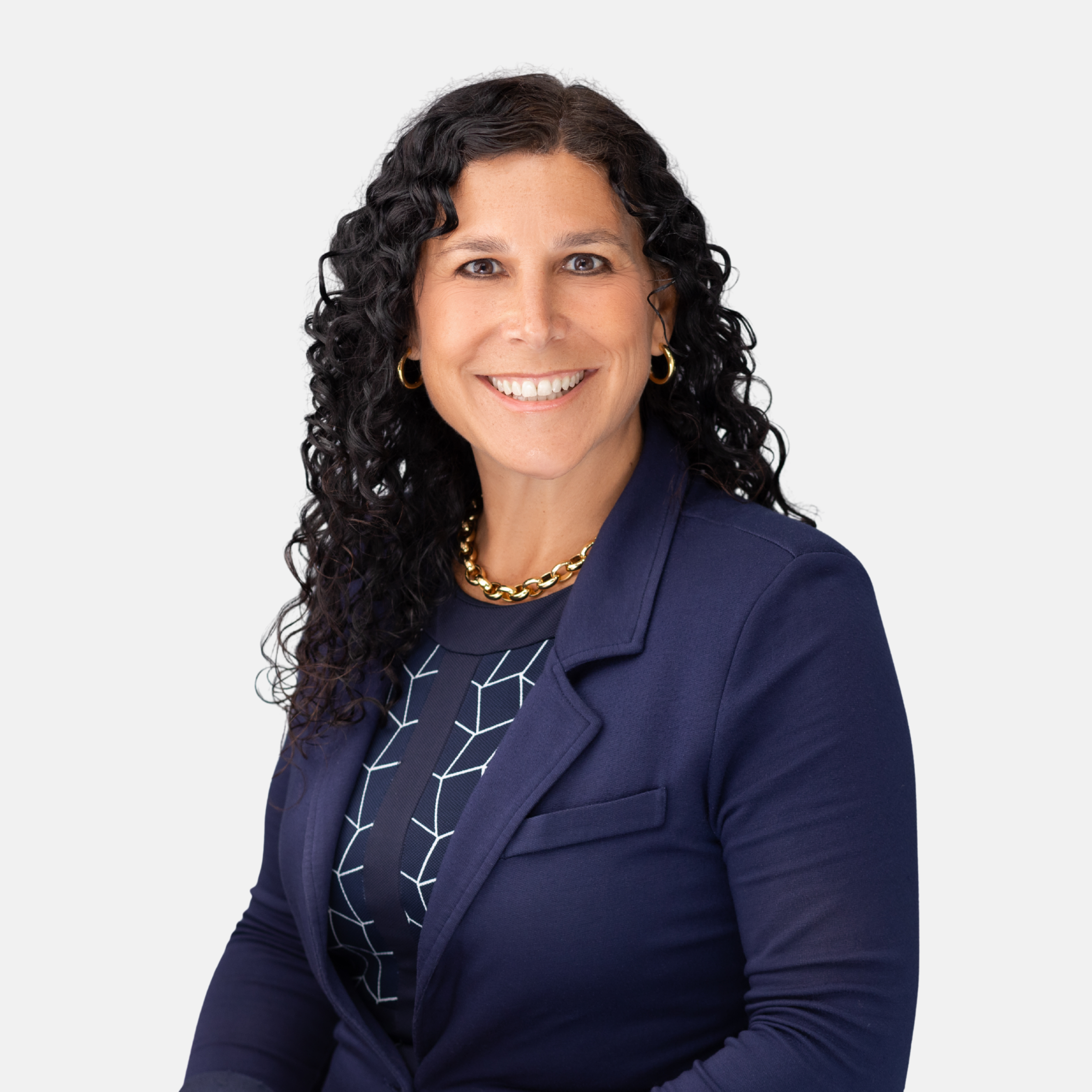 Headshot of Kimberly M. Melvin with long dark curly hair, wearing a dark blue blazer, patterned top, and gold chain necklace, smiling against a light background