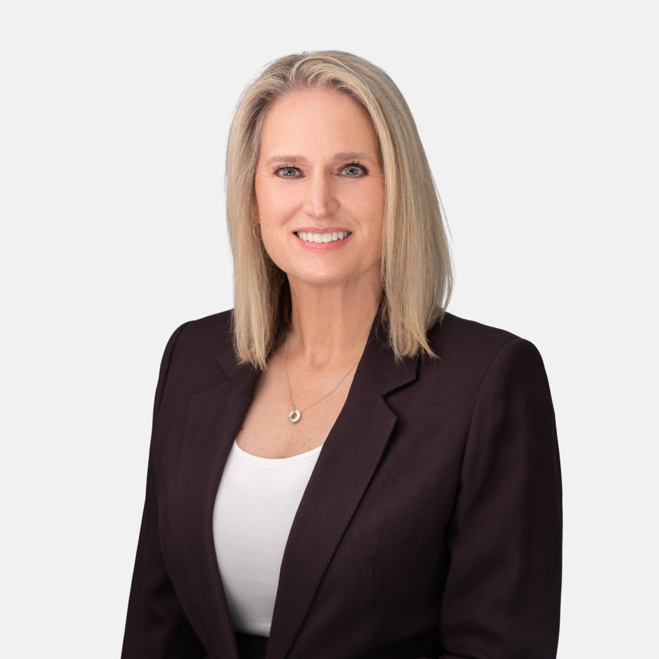 Headshot of Leslie A. Platt with blonde hair, wearing a dark blazer, white top, and necklace, smiling against a light background