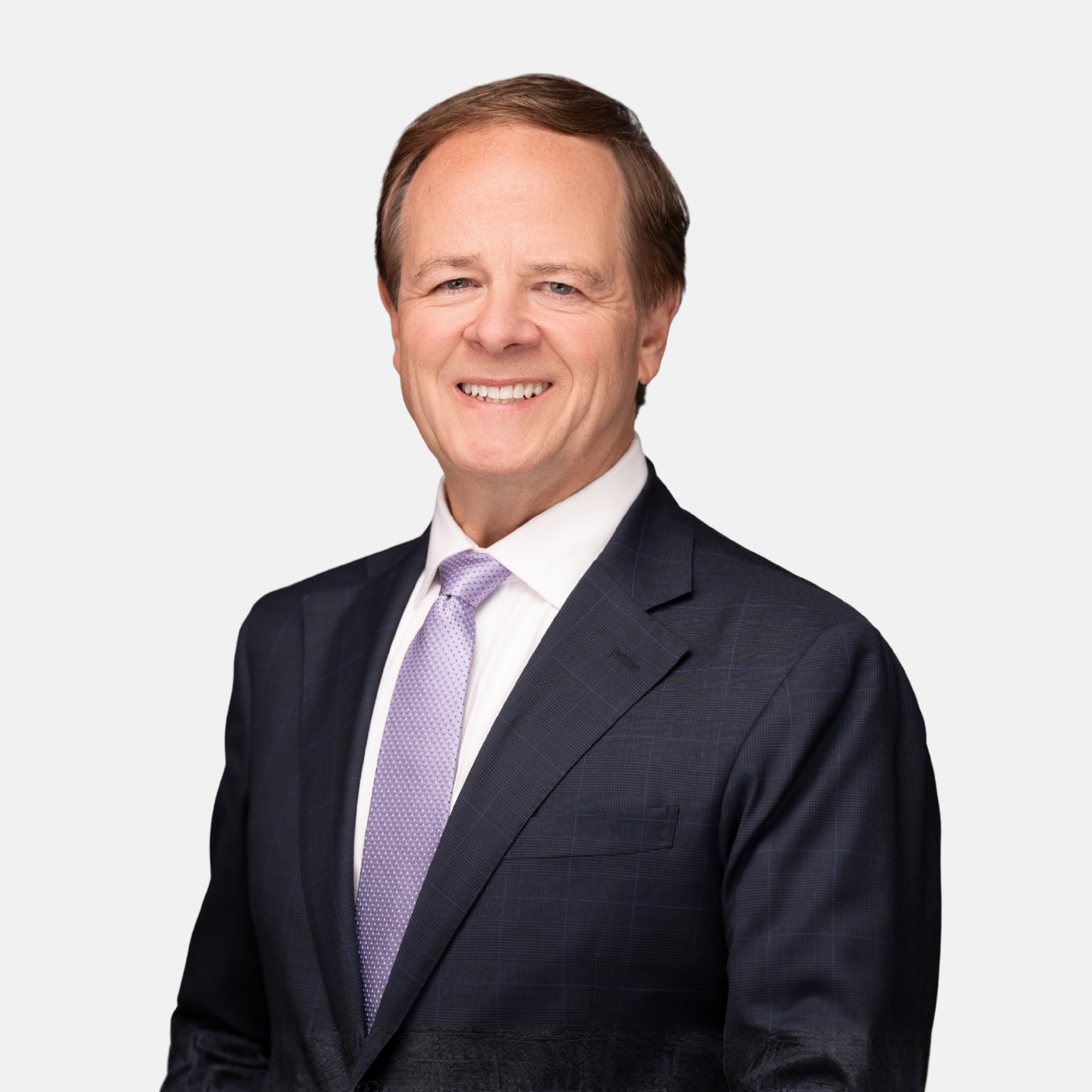 Headshot of Kenneth E. Ryan with short brown hair, wearing a dark suit, light shirt, and patterned purple tie, smiling against a light background