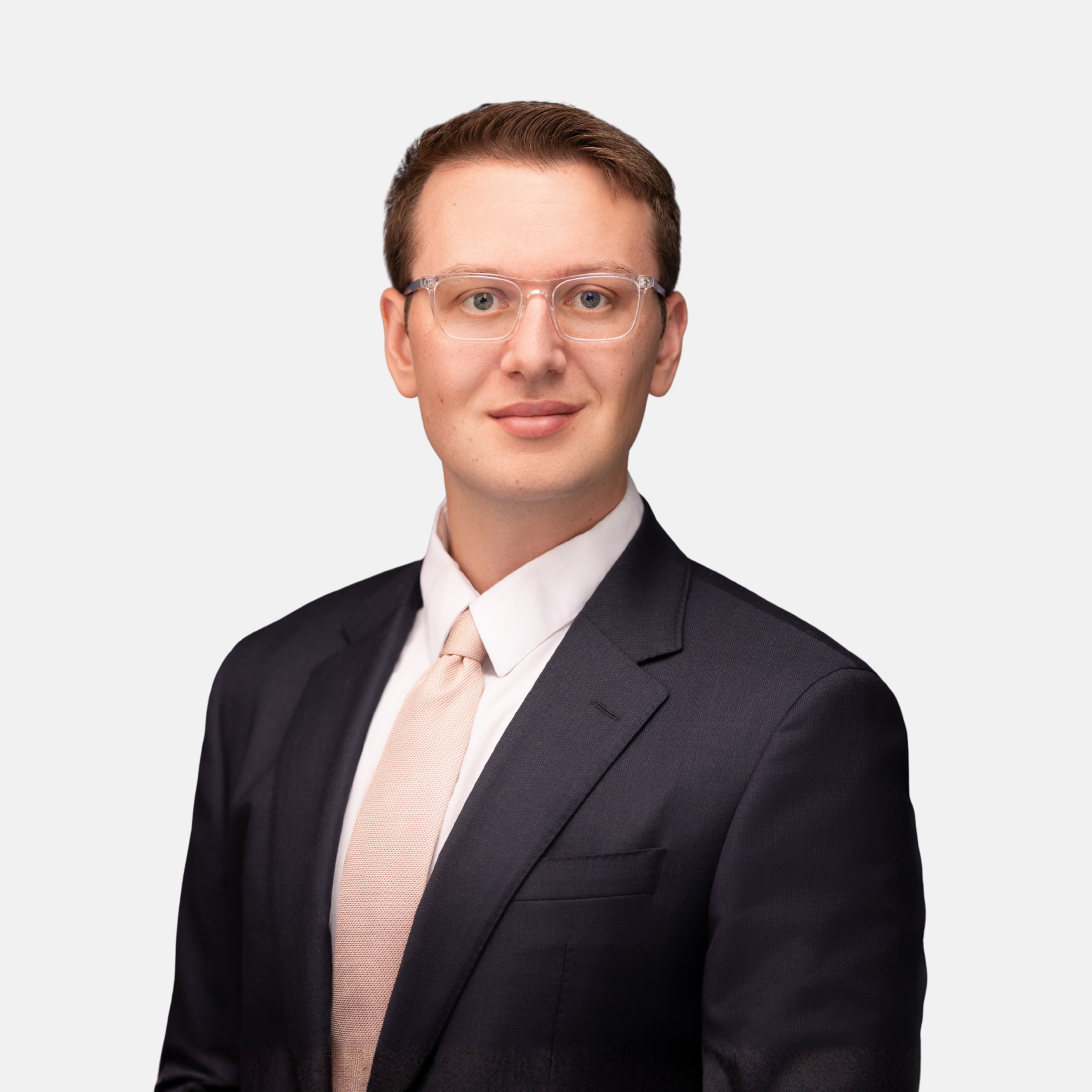Headshot of Thomas B. Boley with short brown hair and glasses, wearing a dark suit, light shirt, and tie, smiling against a light background